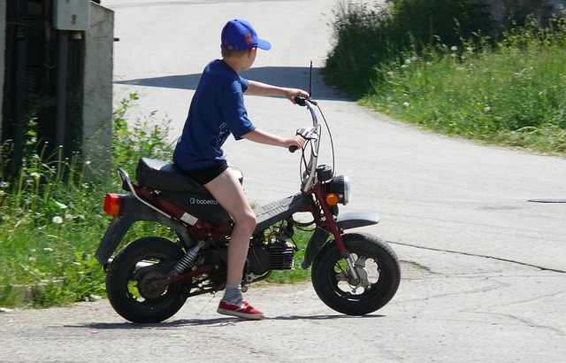 kluk v modrém tričku a modré kšiltovce sedící na malém motocyklu 